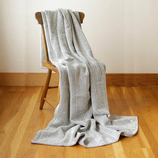 A dark navy blue and white herringbone pattern throw blanket draped over a wooden chair on a light wood floor against a neutral beige wall.